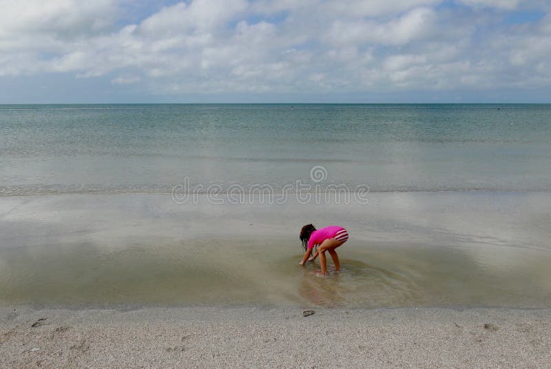 Mädchen, das vorbei in seichtes Wasser im ruhigen Ozeanwasser verbiegt stockbild Mädchen, das vorbei in seichtes Wasser im ruhigen Ozeanwasser verbiegt stockbild