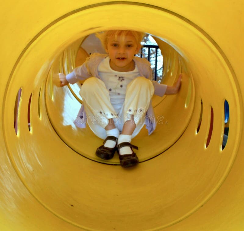 A little girl playing sliding down a tubular yellow slide in a park. A little girl playing sliding down a tubular yellow slide in a park.