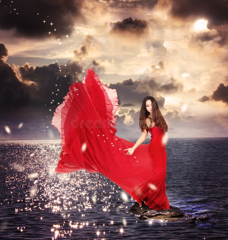 Mädchen im roten Kleid, das auf Ozean-Felsen steht