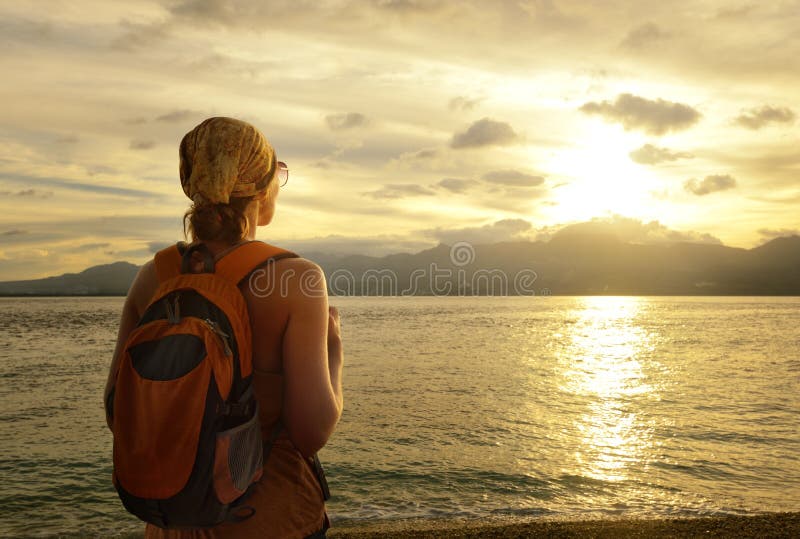 Woman a backpack looking at the sunset behind the mountains leaving. Woman a backpack looking at the sunset behind the mountains leaving