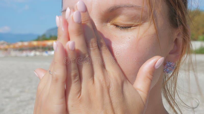 Mädchen schmiert ihre Gesichtshaut mit sunblock Rahm bei der Stellung auf einem sandigen Strand.