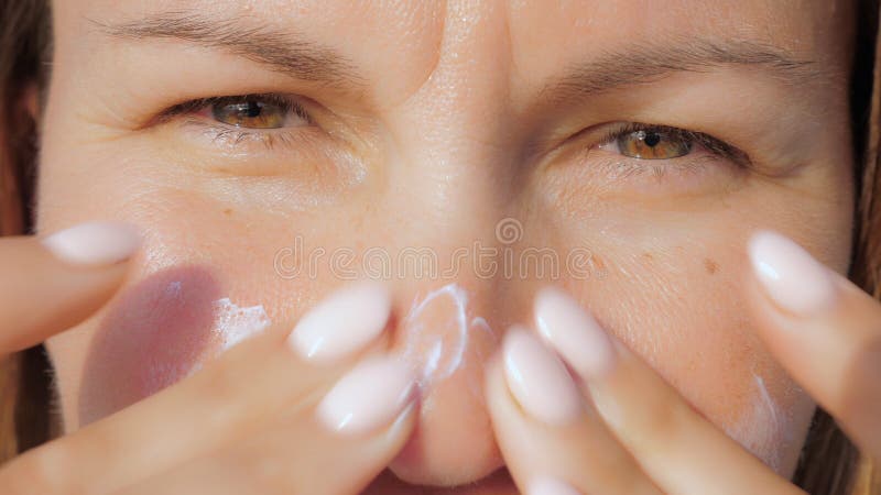 Mädchen schmiert ihre Gesichtshaut mit sunblock Rahm bei der Stellung auf einem Strand