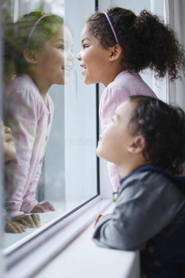 Mädchen Schwestern und schauen nach einem Fenster zu Hause, um Neugier zu verbinden und mit Lächeln und Reflexion zuzusehen. Kinde lizenzfreie stockfotografie