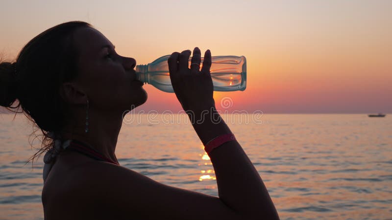 Mädchen trinkt Wasser aus dem See- oder Ozeanufer bei Sonnenuntergang.