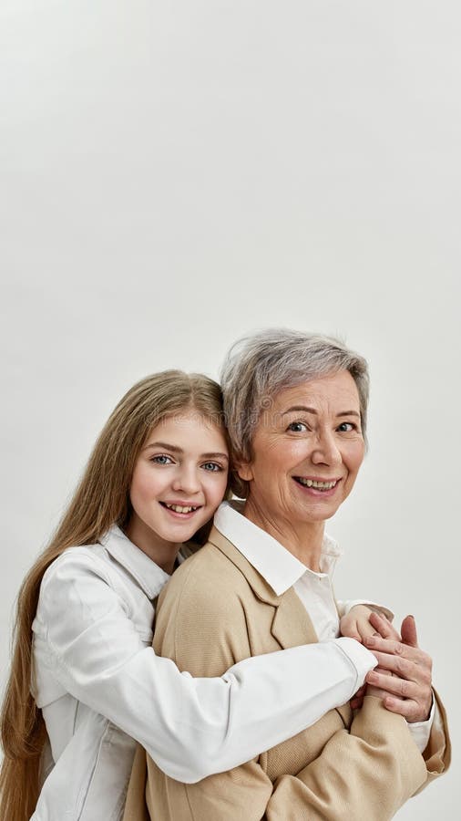 Mädchen umarmt Oma auf weißem Hintergrund im Studio. Enkelin umarmt Großmutter auf weißem Hintergrund im Studio. Alterskonzept. familiäre Beziehung und Nähe. Lächelndes Kaukasisches Mädchen und graue Haare Frauen schauen Kamera an. Kopierraum