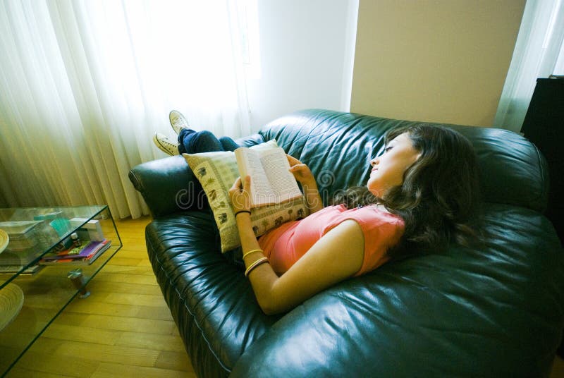 A view of a young girl reclining on a sofa or couch, reading a book. A view of a young girl reclining on a sofa or couch, reading a book.