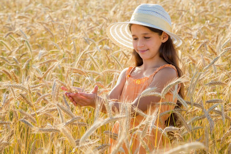 Girl in hat looking to spica of wheat in hads, standing on field. Girl in hat looking to spica of wheat in hads, standing on field