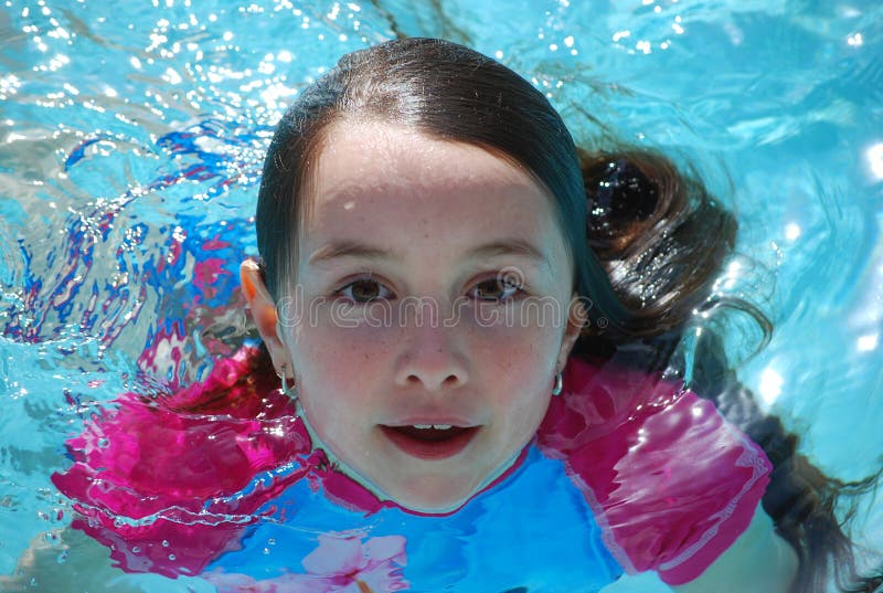 A young girl with brown hair and eyes swimming in a pool just coming up from being underwater. A young girl with brown hair and eyes swimming in a pool just coming up from being underwater.