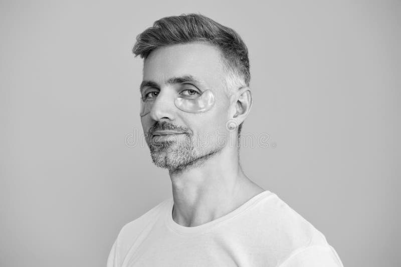 Män med applicerat fuktande under ögonanti- rynkplåster. Etiska skönhetskincenter. Man med skrynklingande ögonplåster royaltyfri bild