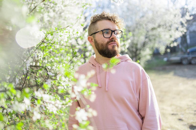 Male bearded guy standing under branches with flowers of blooming almond or cherry tree in spring garden. Spring blossom. Copy space. Male bearded guy standing under branches with flowers of blooming almond or cherry tree in spring garden. Spring blossom. Copy space