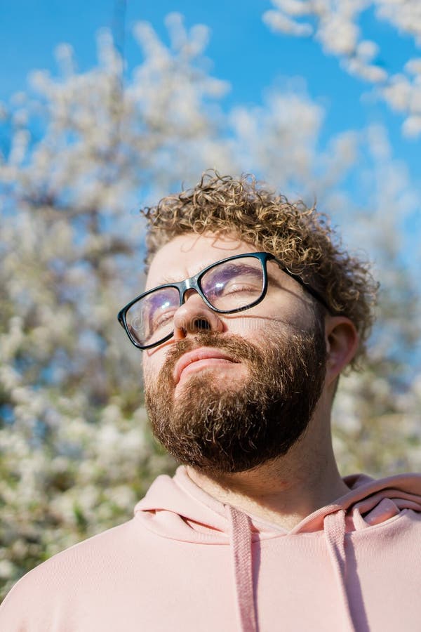 Male bearded guy standing under branches with flowers of blooming almond or cherry tree in spring garden. Spring blossom. Copy space. Male bearded guy standing under branches with flowers of blooming almond or cherry tree in spring garden. Spring blossom. Copy space