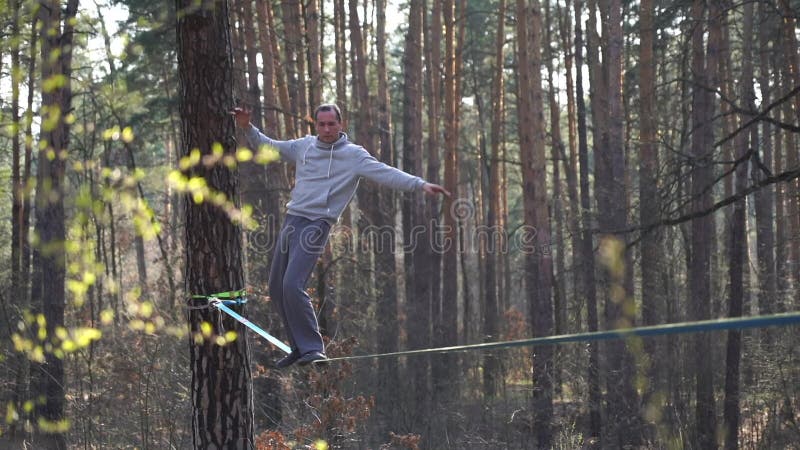 Människan som hoppar och gör trick på slackline i skogen i långsam rörelse lager videofilmer