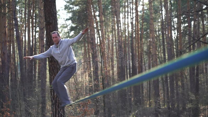 Människan som hoppar och gör trick på slackline i skogen i långsam rörelse arkivfilmer