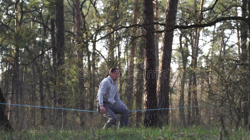 Människan som hoppar och gör trick på slackline i skogen i långsam rörelse lager videofilmer