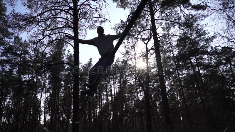 Människan som hoppar och gör trick på slackline i skogen i långsam rörelse lager videofilmer