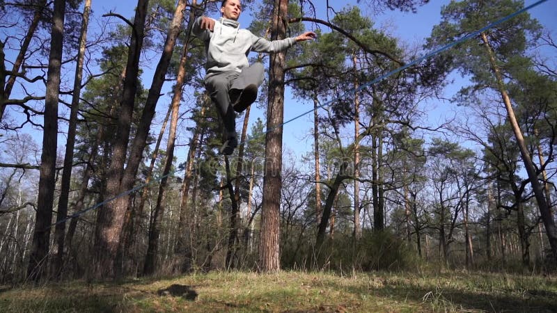 Människan som hoppar och gör trick på slackline i skogen i långsam rörelse stock video
