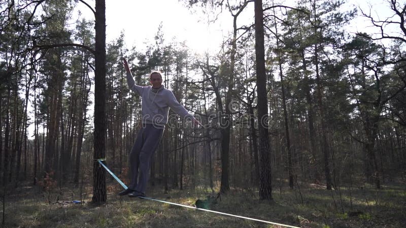 Människan som hoppar och gör trick på slackline i skogen i långsam rörelse arkivfilmer