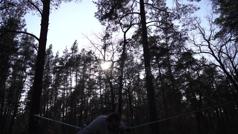 Människan som hoppar och gör trick på slackline i skogen i långsam rörelse lager videofilmer