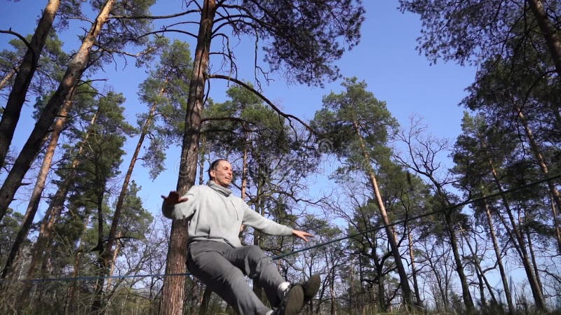 Människan som hoppar och gör trick på slackline i skogen i långsam rörelse arkivfilmer