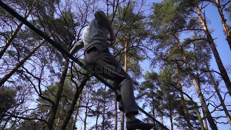 Människan som hoppar och gör trick på slackline i skogen i långsam rörelse arkivfilmer