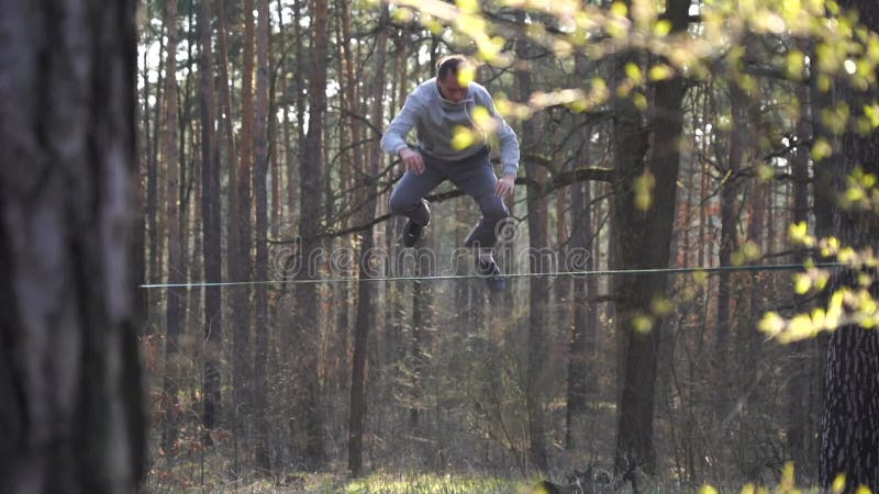 Människan som hoppar och gör trick på slackline i skogen i långsam rörelse stock video