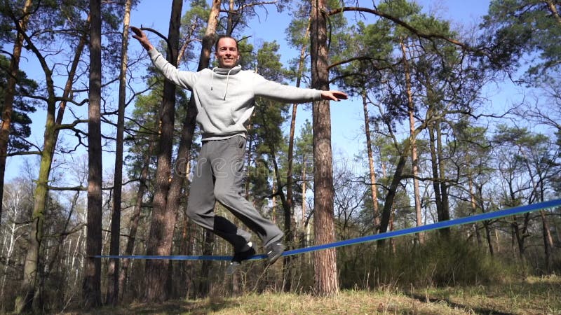 Människan som hoppar och gör trick på slackline i skogen i långsam rörelse lager videofilmer