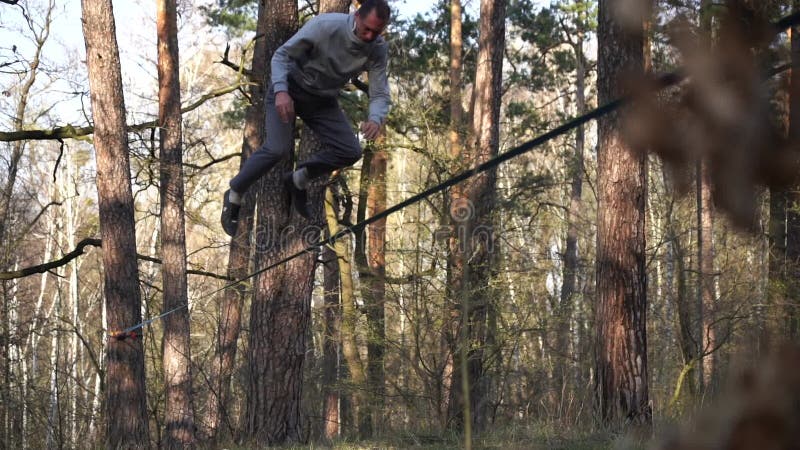 Människan som hoppar och gör trick på slackline i skogen i långsam rörelse arkivfilmer