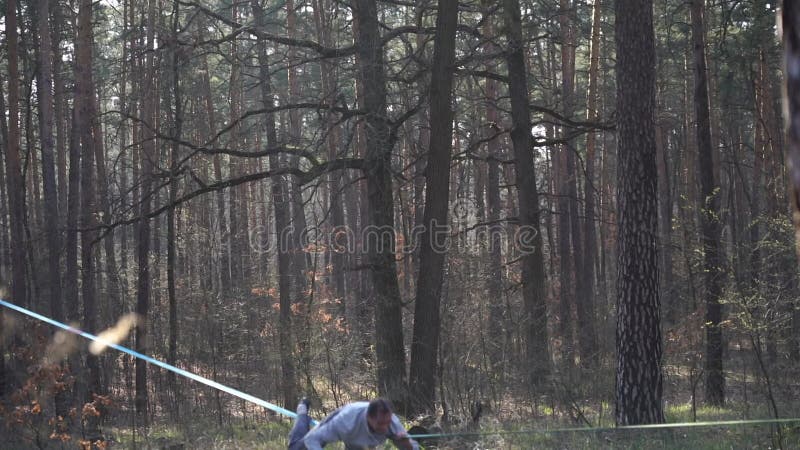 Människan som hoppar och gör trick på slackline i skogen i långsam rörelse lager videofilmer
