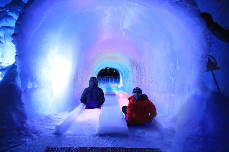 A picture of People sliding down an ice slide in a tunnel with rainbow colors in winter. A picture of People sliding down an ice slide in a tunnel with rainbow colors in winter