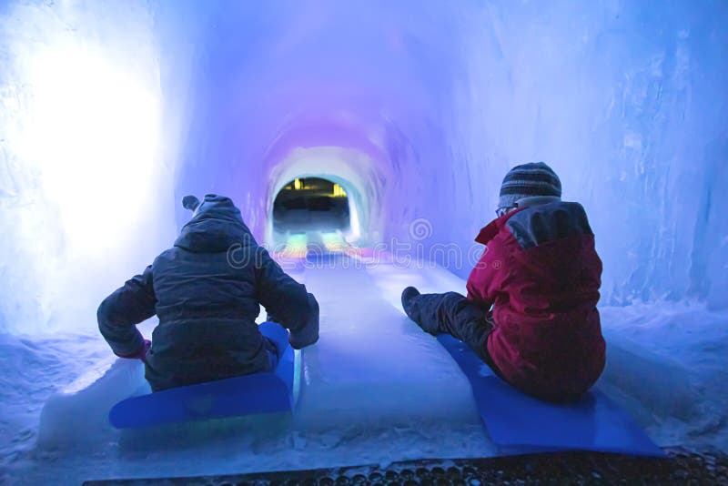 A picture of People sliding down an ice slide in a tunnel with rainbow colors in winter. A picture of People sliding down an ice slide in a tunnel with rainbow colors in winter