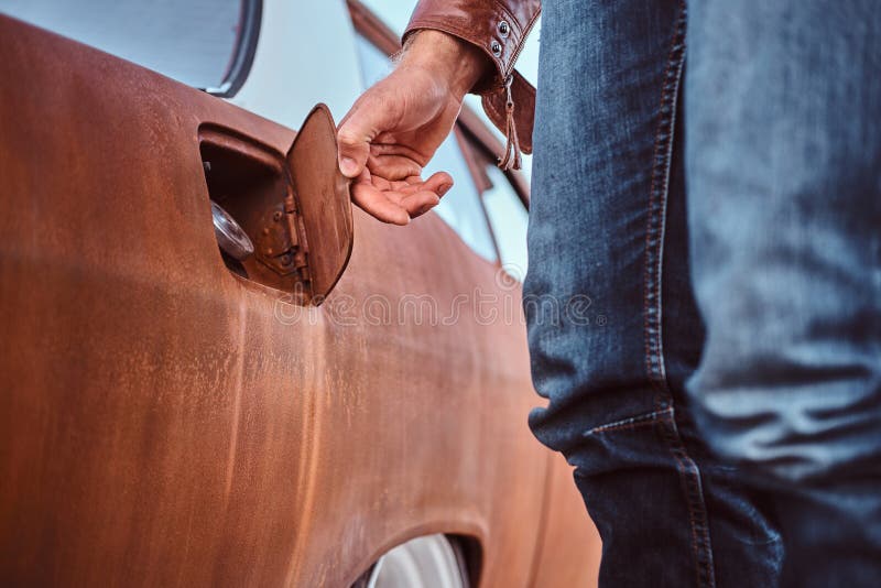 Cropped photo of a male hand opens the gas cap of a tuned retro car for refueling. Cropped photo of a male hand opens the gas cap of a tuned retro car for refueling.