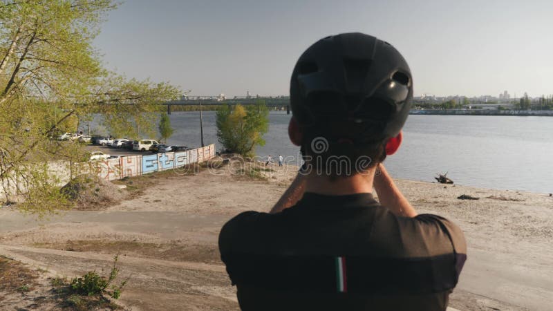 Männliche Radfahrerholding-Telefonkamera und nehmen Bilder von Fluss, von Brücke und von Stadt Der bärtige Radfahrer, der Fotos m