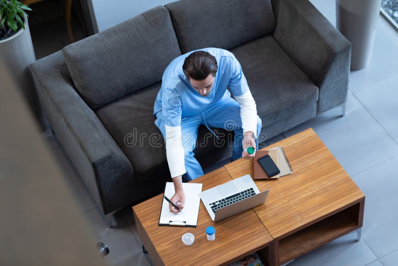 Männlicher Doktor, der auf Klemmbrett ins Krankenhauslobby schreibt stockbild Männlicher Doktor, der auf Klemmbrett ins Krankenhauslobby schreibt stockbild