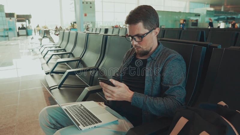 Männlicher Passagier, der in Wartehalle im Flughafen sitzen und simsende sms durch Smartphone