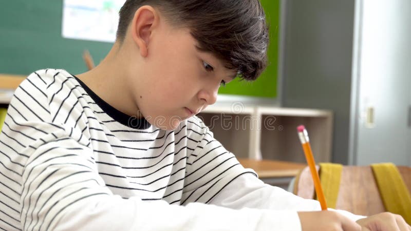 Männlicher Student, der am Schreibtisch im Klassenzimmerschreiben im Notebook in der Prüfung sitzt