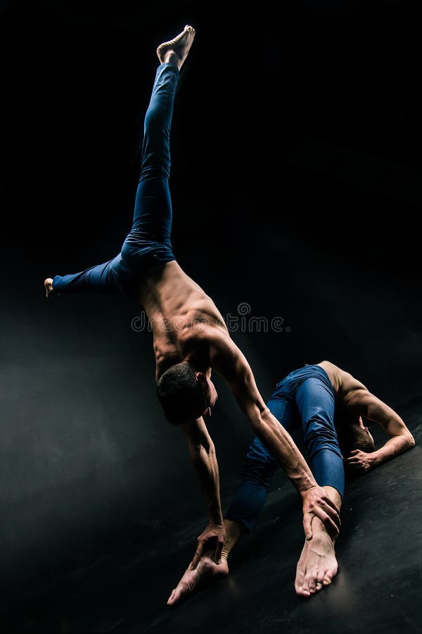 Männliches akrobatisches Duo führt einen schwierigen Balanceakt auf einem dunklen Hintergrund durch stockbild Männliches akrobatisches Duo führt einen schwierigen Balanceakt auf einem dunklen Hintergrund durch stockbild