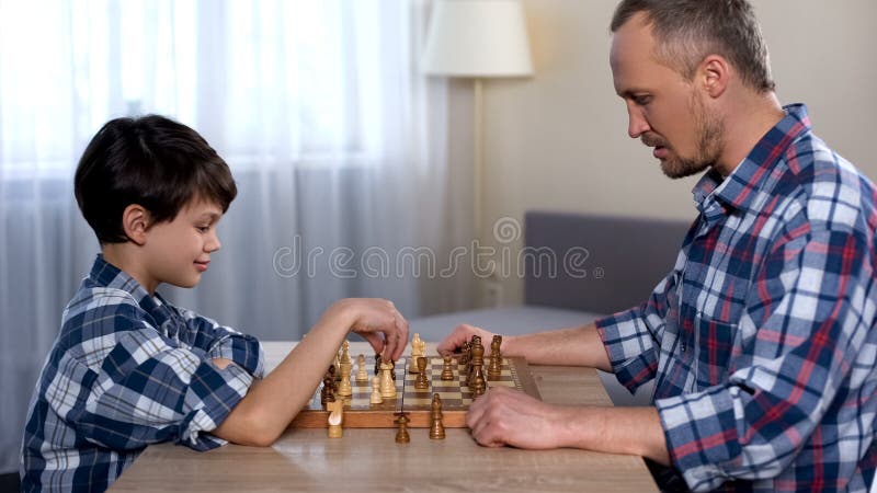 Männliches Kinderbewegendes Schach an Bord, Spiel mit Vater spielend, Lieblingshobby stockfotos Männliches Kinderbewegendes Schach an Bord, Spiel mit Vater spielend, Lieblingshobby stockfotos