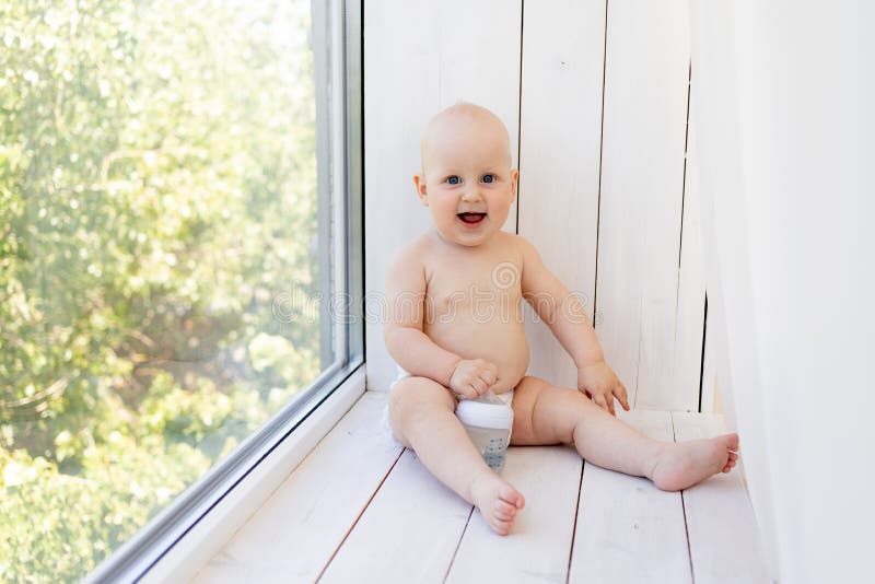8 månaders barnpojke som sitter i blöjor på fönsterkanten och tittar in på det avstånd som en plats för text royaltyfri foto
