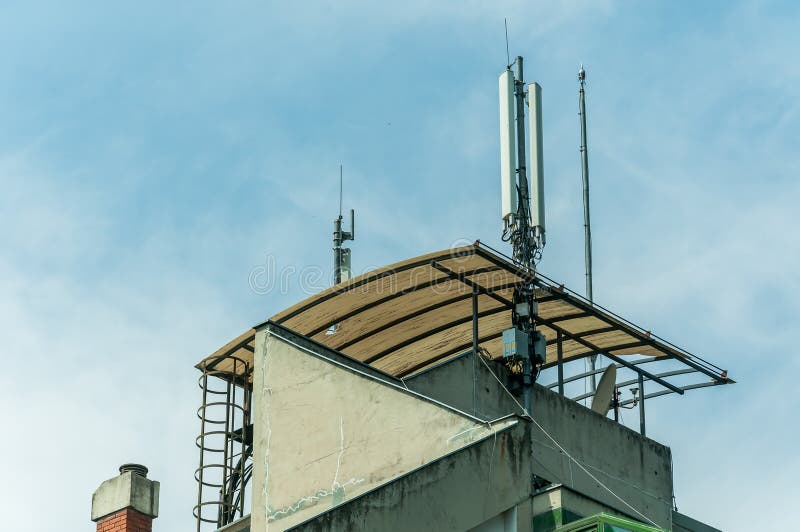 Många antenner för telekommunikationmobiltelefonmottagare på taköverkanten av den bostads- byggnaden med bakgrund för blå himmel, royaltyfria bilder Många antenner för telekommunikationmobiltelefonmottagare på taköverkanten av den bostads- byggnaden med bakgrund för blå himmel, royaltyfria bilder