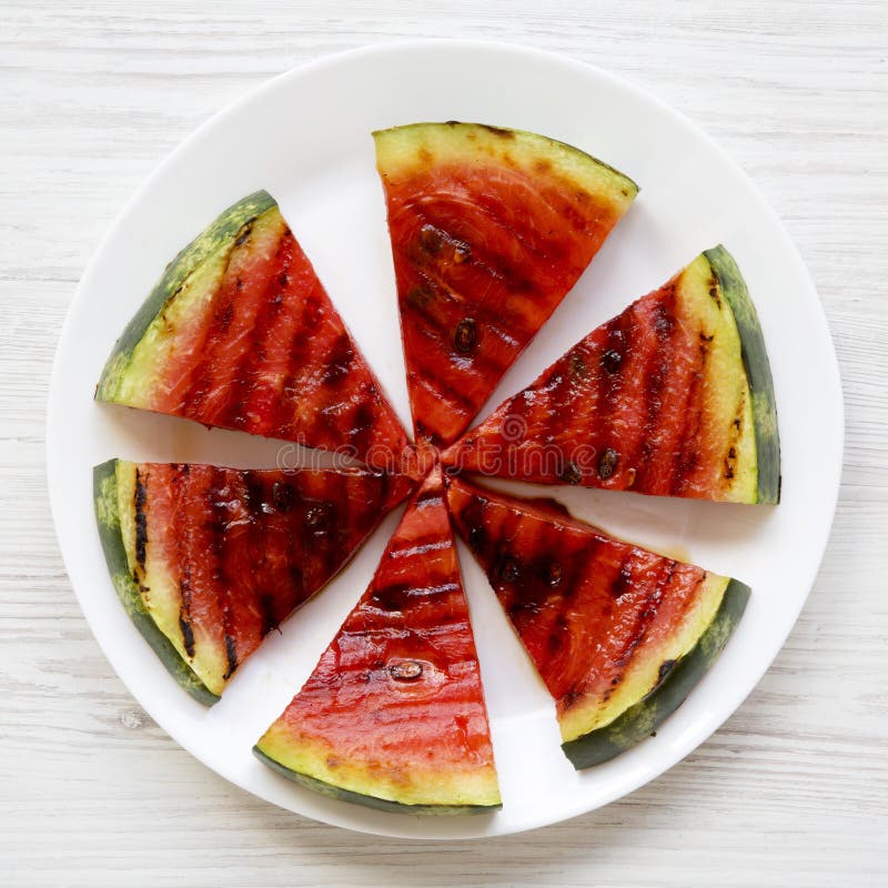 Många skivor av den nya mogna grillade vattenmelon på en vit rund platta över vit träyttersida, bästa sikt Sund sommarfrukt arkivbild Många skivor av den nya mogna grillade vattenmelon på en vit rund platta över vit träyttersida, bästa sikt Sund sommarfrukt arkivbild