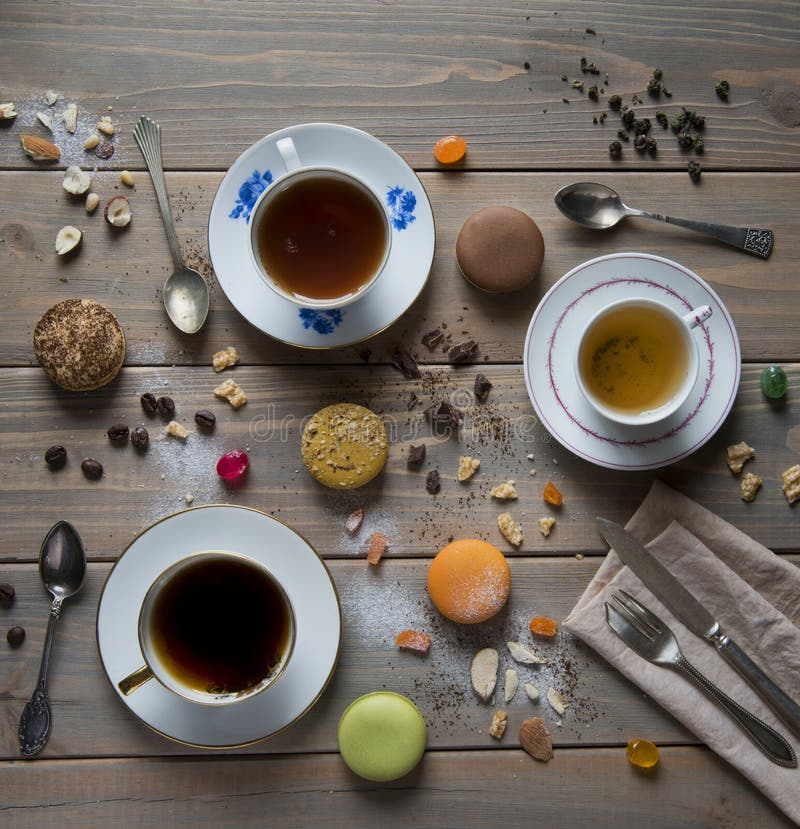 Mångfärgade Macarons, koppar med svart och grönt te och med kaffe, tappningskedar, gaffel och kniv på en trätabell med variou arkivfoto