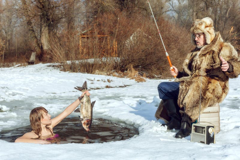 Young girl emerged from the ice-hole and stretches the fish to an elderly fisherman. Young girl emerged from the ice-hole and stretches the fish to an elderly fisherman