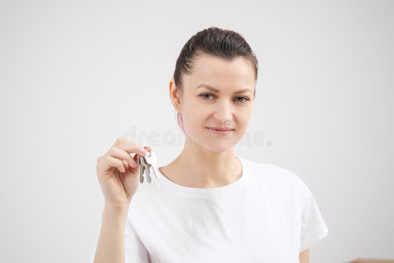 Młoda piękna brunetki dziewczyna w koszulki białych chwytach w jej rękach klucze nowy dom przeciw tłu, fotografia royalty free Młoda piękna brunetki dziewczyna w koszulki białych chwytach w jej rękach klucze nowy dom przeciw tłu, fotografia royalty free
