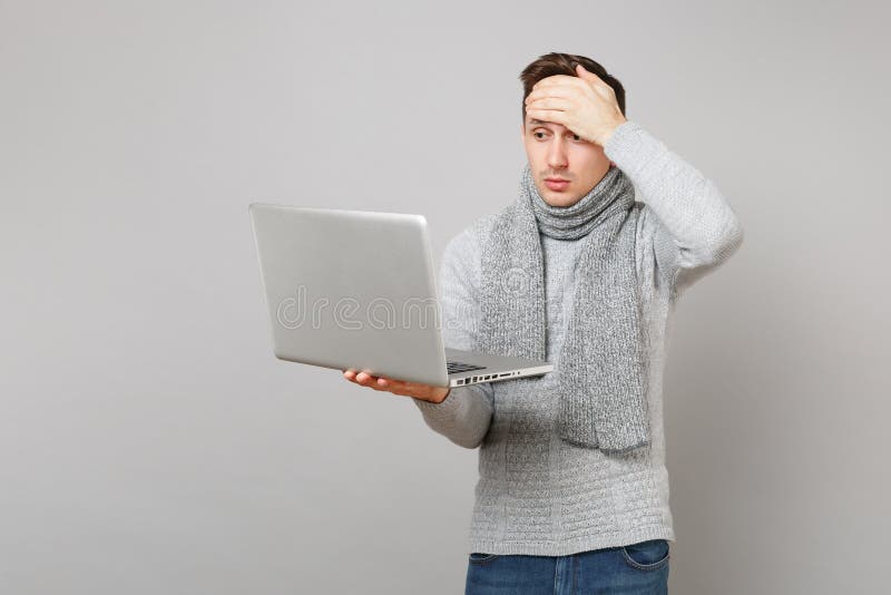 Młody człowiek w szarym pulowerze, szalik pracuje na laptopu komputeru osobistego komputerze, stawiająca ręka na czole odizolowyw fotografia stock Młody człowiek w szarym pulowerze, szalik pracuje na laptopu komputeru osobistego komputerze, stawiająca ręka na czole odizolowyw fotografia stock