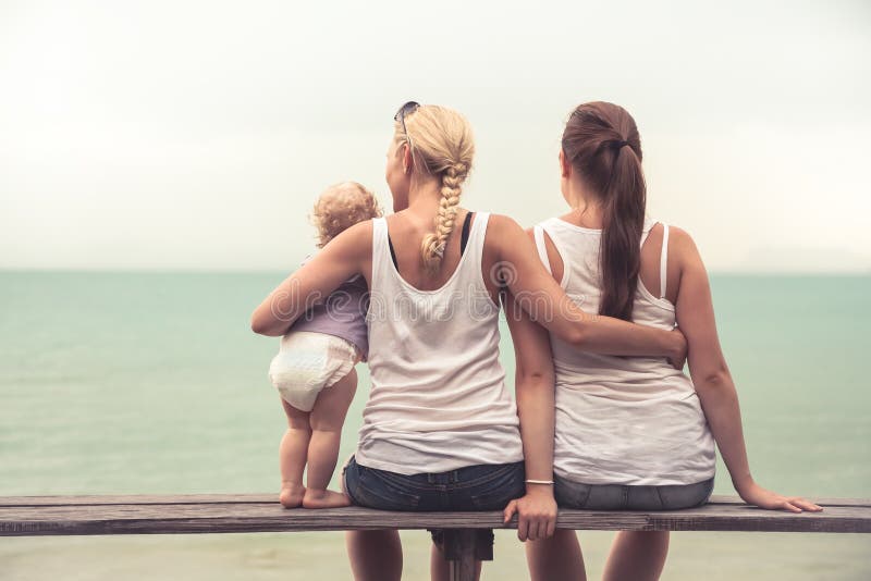 Mère affectueuse embrassant ses enfants s'asseyant sur le banc en bois à la plage tropicale pendant des vacances Ils examinant en image stock Mère affectueuse embrassant ses enfants s'asseyant sur le banc en bois à la plage tropicale pendant des vacances Ils examinant en image stock