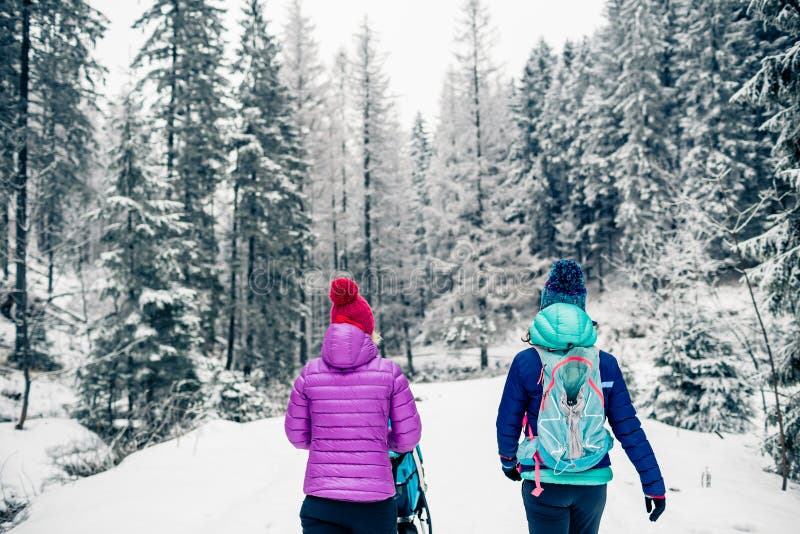 Mère avec le promeneur de bébé appréciant la maternité dans la forêt d'hiver photo stock Mère avec le promeneur de bébé appréciant la maternité dans la forêt d'hiver photo stock