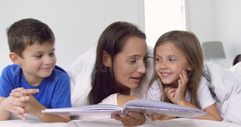 Mère avec ses enfants lisant le livre d'histoire dans la chambre à coucher à la maison 4k