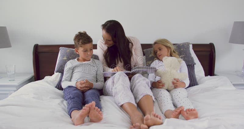 Mère avec ses enfants lisant le livre d'histoire dans la chambre à coucher à la maison 4k