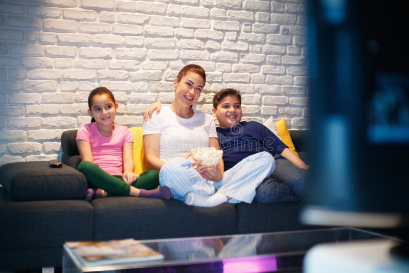 Mère célibataire et enfants regardant la TV la nuit image stock Mère célibataire et enfants regardant la TV la nuit image stock