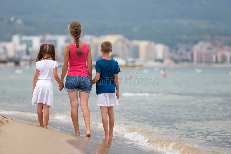 Mère et deux enfants, fils et fille, marchant ensemble sur la plage de sable en été les pieds nus dans l'eau de mer avec des vagu image libre de droits Mère et deux enfants, fils et fille, marchant ensemble sur la plage de sable en été les pieds nus dans l'eau de mer avec des vagu image libre de droits